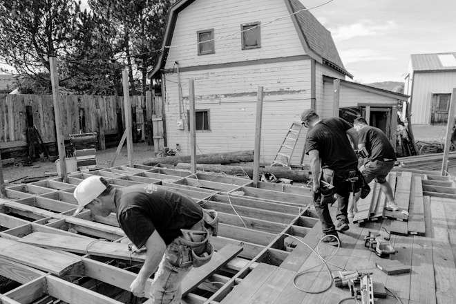 Carpenters frame a wooden deck outside a house