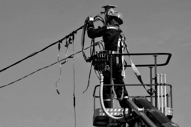 A lineworker in a harness works on overhead power lines from a bucket truck