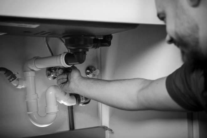 A plumber's hands fitting a drain trap under a sink