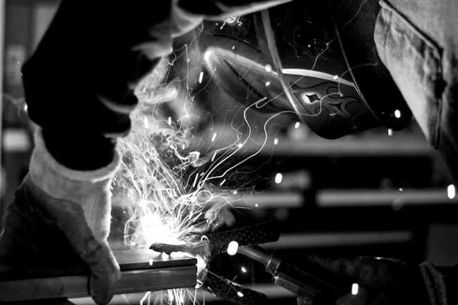 A welder in a helmet and gloves throws sparks while welding steel